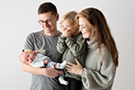 Mädchen hält den Mund zu, Eltern schauen auf das Baby